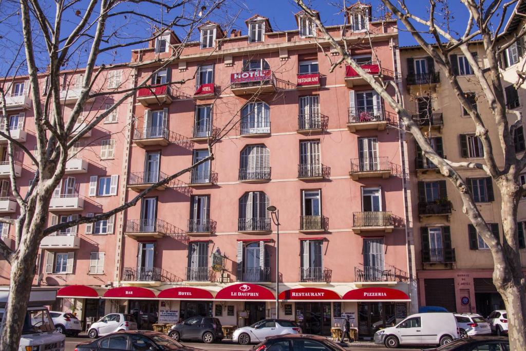 a large pink building with cars parked in front of it at Hotel le Dauphin in Ajaccio