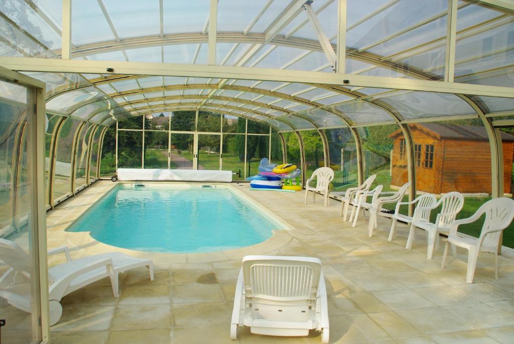 a swimming pool in a greenhouse with chairs around it at La Grimodière in Ranville