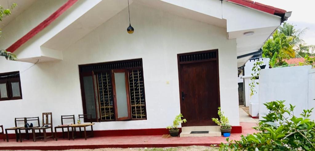une maison blanche avec une porte et des chaises en bois dans l'établissement Madiha home staying, à Matara
