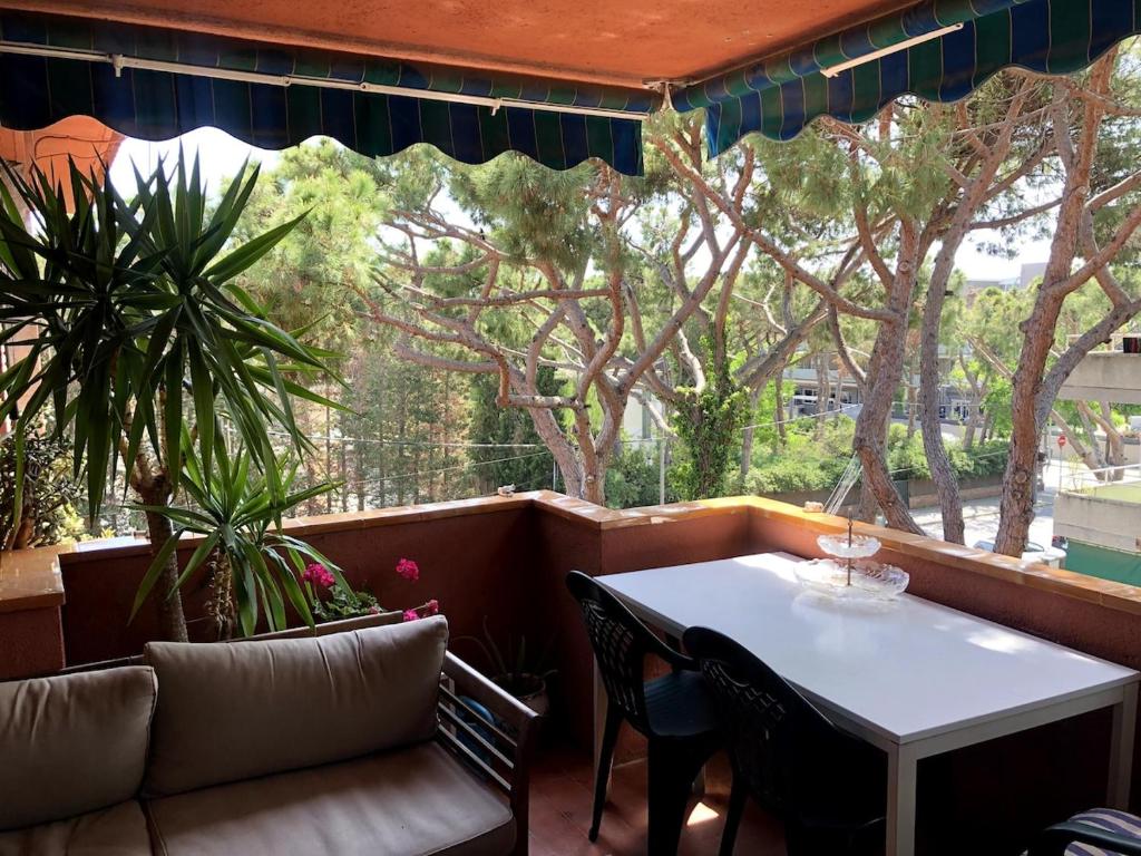 Un porche con mesa y sillas y árboles. en Beach apartment 2 terraces with parking, en Castelldefels