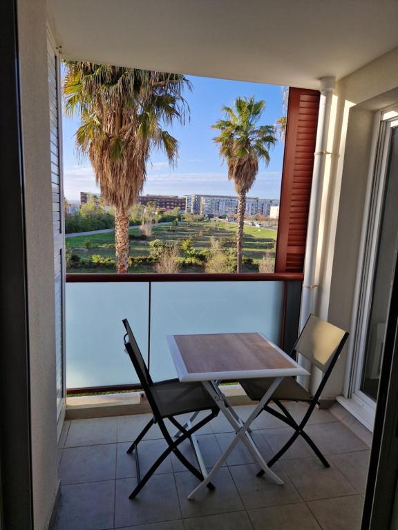 une table et une chaise en face d'une fenêtre bordée de palmiers dans l'établissement Le Grand Large T2 climatisé à 200 m plage, parking, à Sète