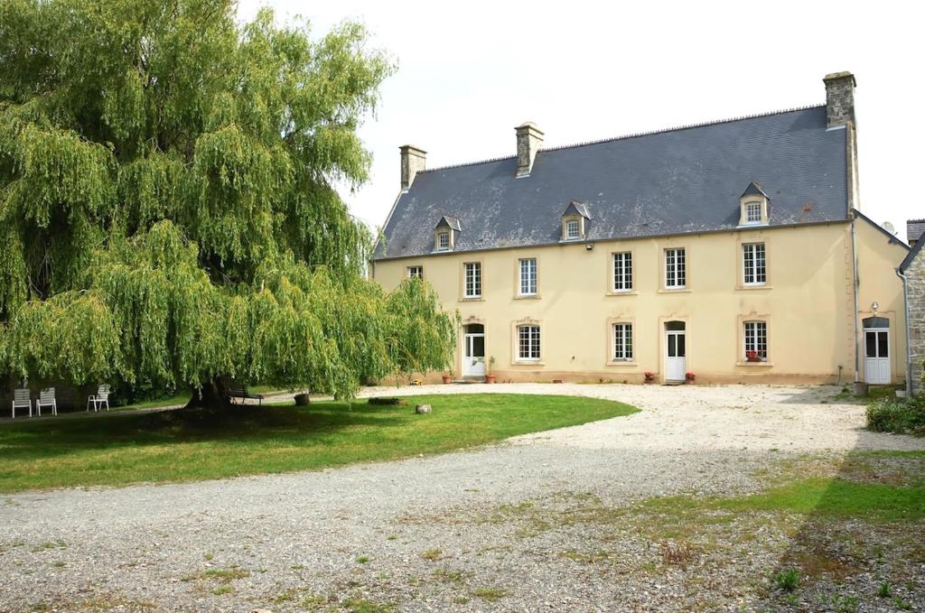 une grande maison jaune avec un arbre en face dans l'établissement La Ferme de Franqueville 'Big Gîte', à Sainte-Marie-du-Mont