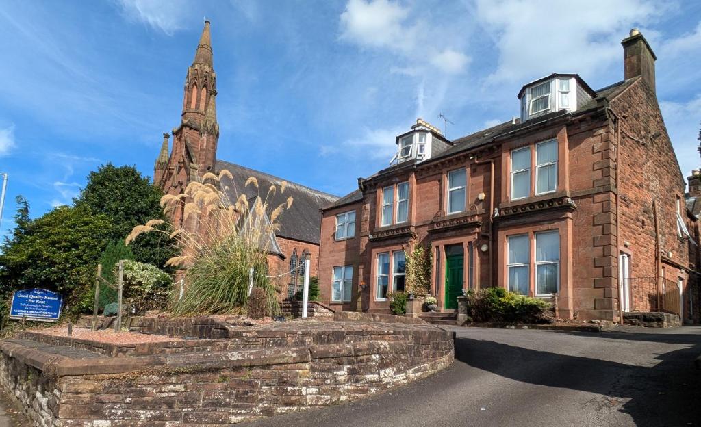 ein altes Backsteingebäude mit einer Kirche im Hintergrund in der Unterkunft Hollybank - ensuite room & use of large shared kitchen in Dumfries