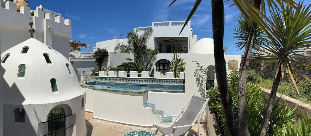 a white house with a swimming pool and palm trees at RIAD OASIS D'ASILAH in Asilah