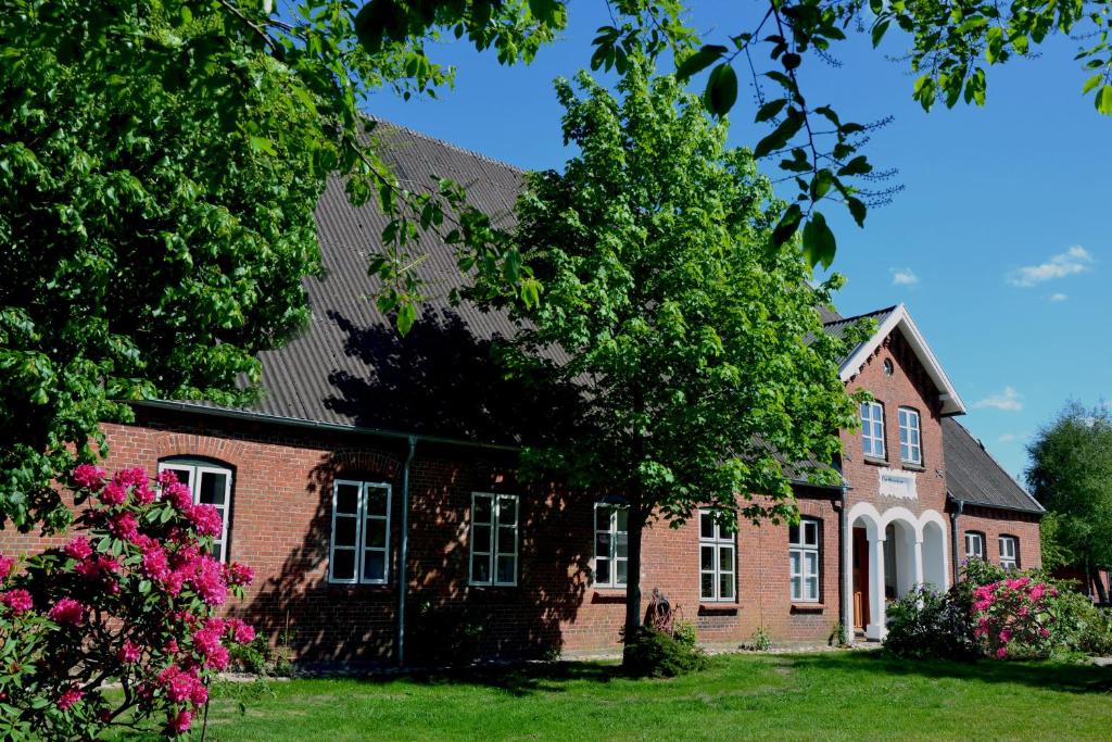 una casa de ladrillo rojo con árboles y flores rosas en Pottkiekerhus, en Luhnstedt