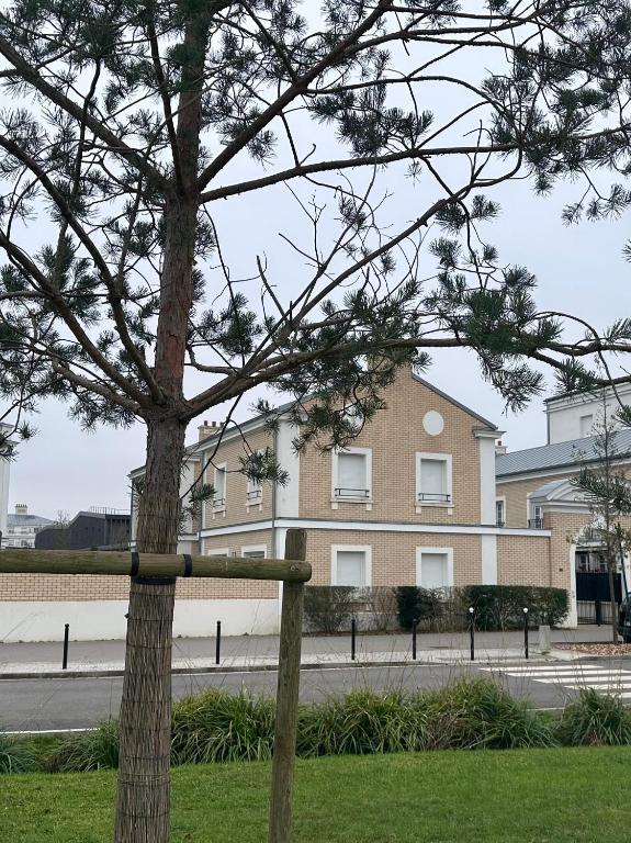 un arbre devant un grand bâtiment dans l'établissement Family's house - Villa proche de la vallée village et Disneyland paris ,2 parkings, air condition, à Serris