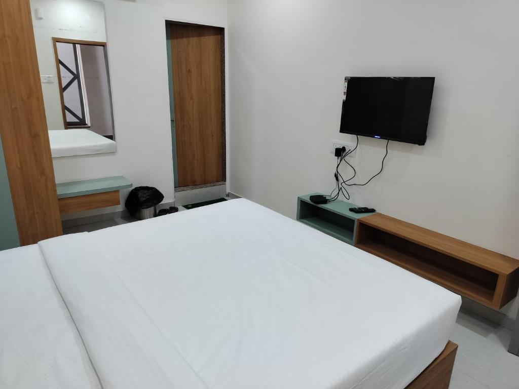 a bedroom with a white bed and a flat screen tv at Hotel Amrutam And Guest House in Tharād