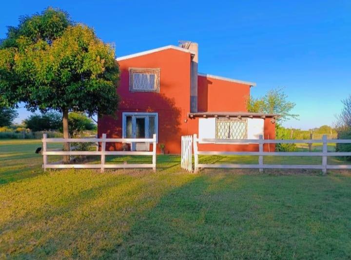 an orange house with a white fence in a field at Chacra CHANCAY in Mercedes