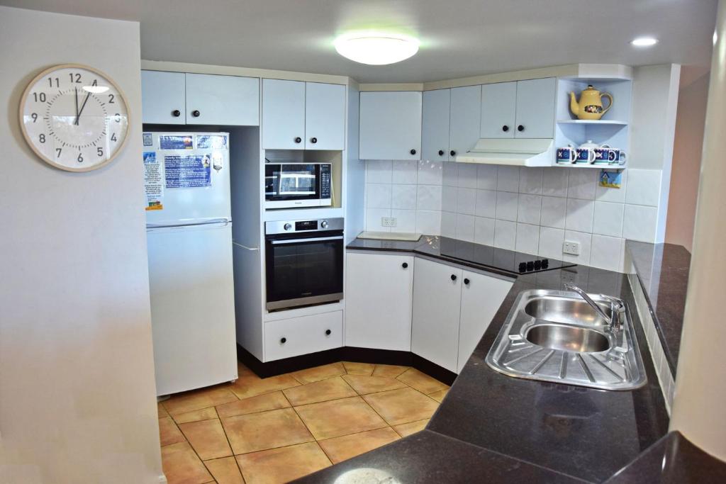 Una cocina con gabinetes blancos y un reloj en la pared. en Ocean Shores Apartment 15 - Bring your own linen., en South West Rocks