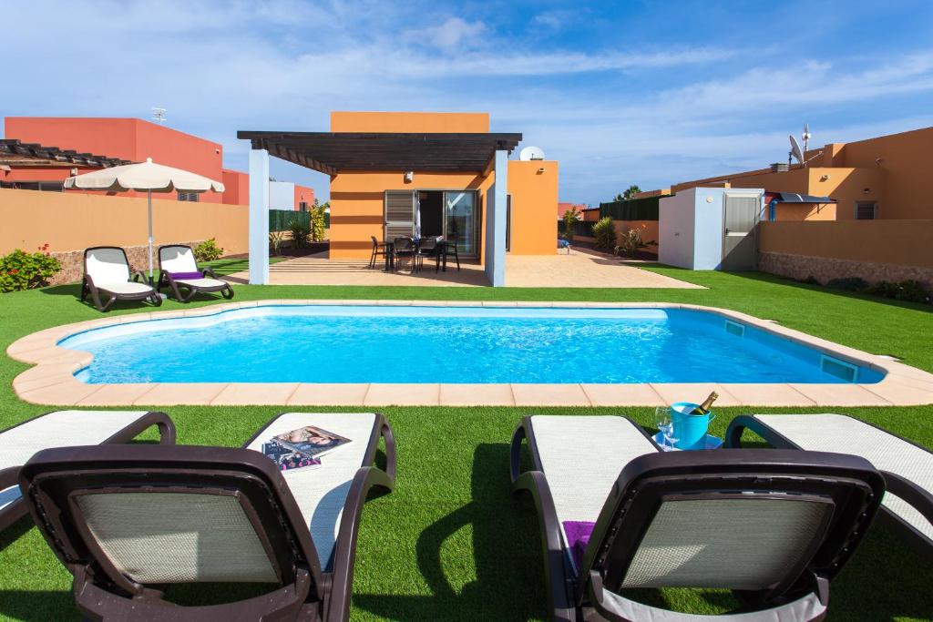 una piscina con 2 sillas y una mesa al lado en Villa con Piscina ,Vista Mar y campo de golf, en Caleta de Fuste