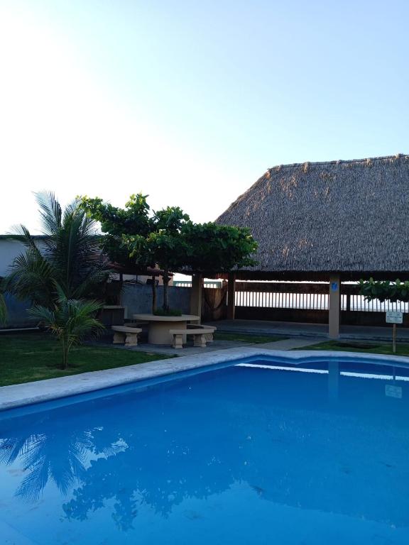 a blue swimming pool with a thatch roof at Rancho Joya Del Mar in Sonsonate