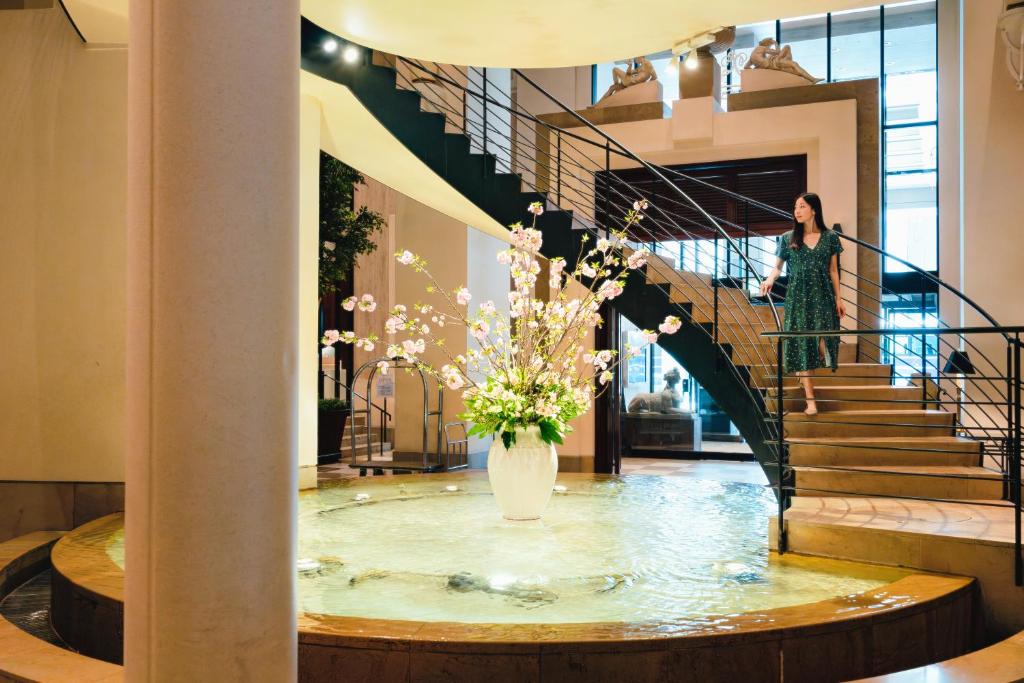 a woman walking down a spiral staircase with a vase of flowers at Hotel Nikko Kanazawa in Kanazawa
