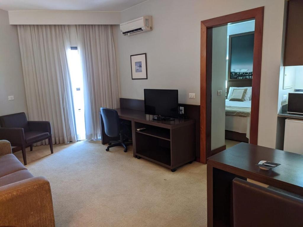a living room with a desk with a television and a living room at Hotel Bonaparte Moderno e versátil in Brasilia