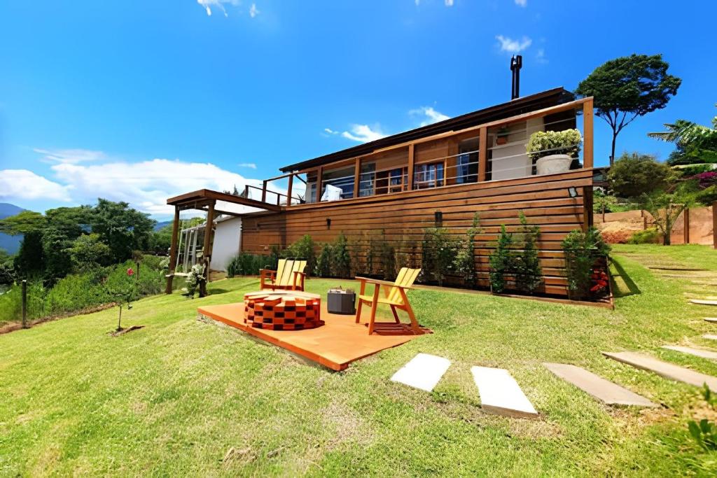 a house on a lawn with two chairs in front of it at Recanto Pôr do Sol com Hido e lareira in Santo Amaro da Imperatriz