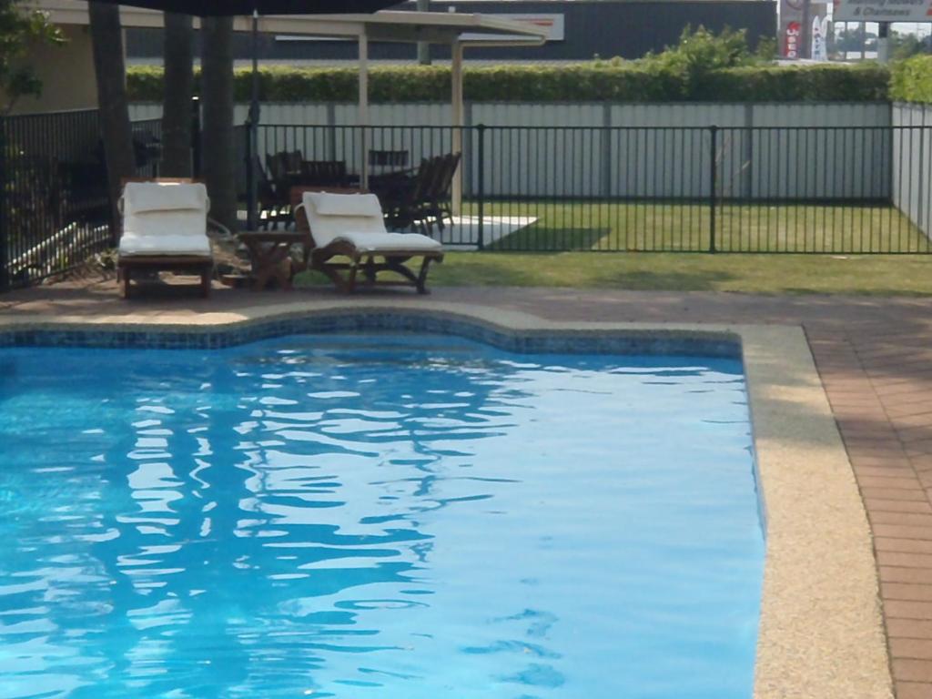 a swimming pool with two chairs and a gazebo at Caravilla Motor Inn in Taree