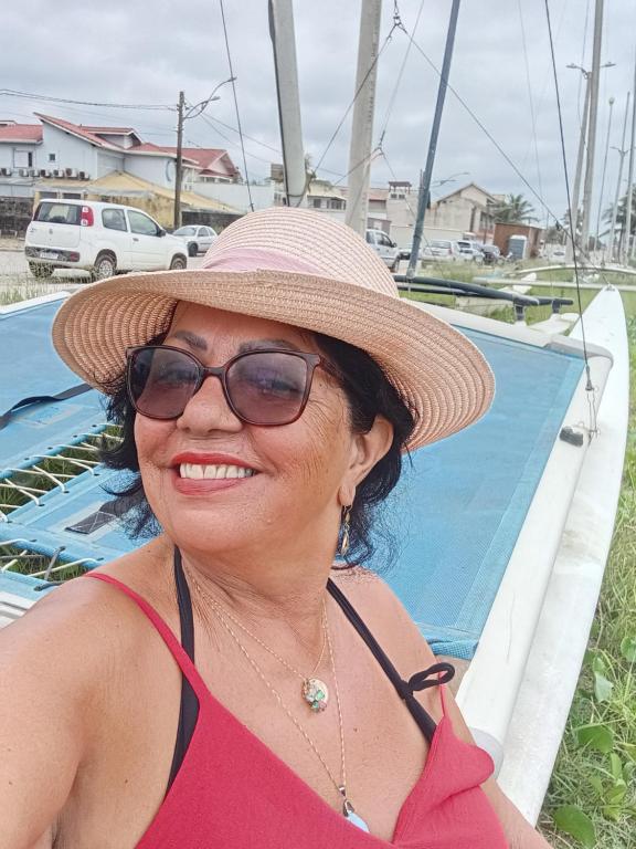 a woman wearing a hat and glasses next to a boat at CANTO DO PARAÍSO Praia RUÍNAS in Peruíbe