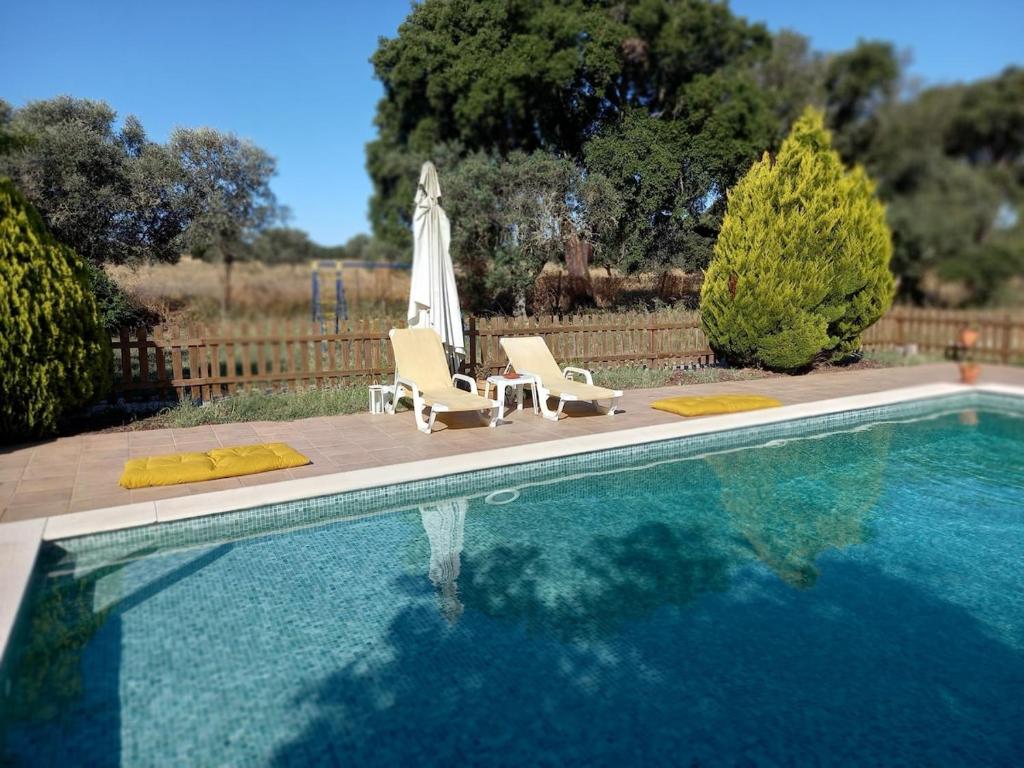 a swimming pool with two chairs and an umbrella at Courela da Anta in Vimieiro