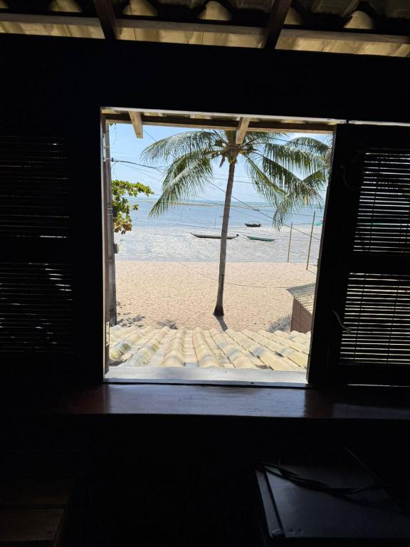a window view of a beach with a palm tree at Igapeba Hospedaria em Moreré in Cairu