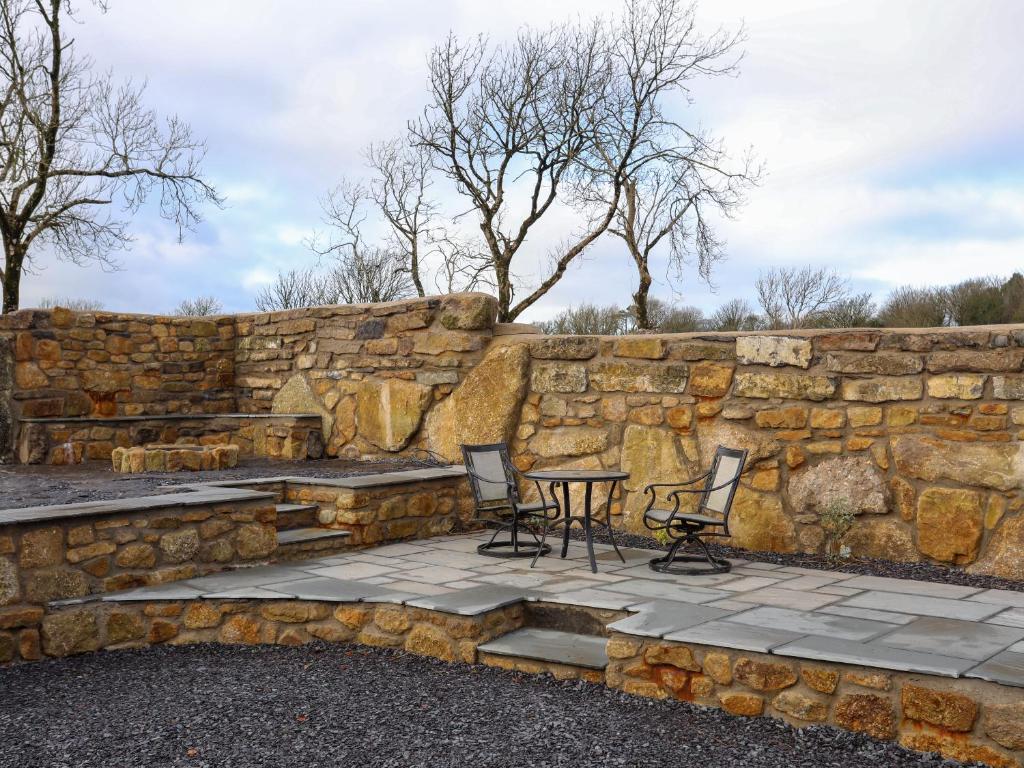 a stone retaining wall with a table and chairs at Ynys Uchaf in Brynteg