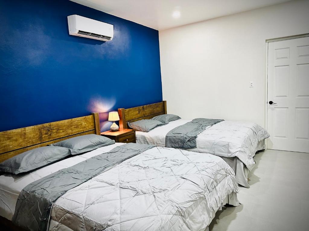 two beds in a bedroom with a blue wall at Eagle Stays Aruba-NEW Stunning One Bedroom Apartment Near Eagle Beach! in Oranjestad