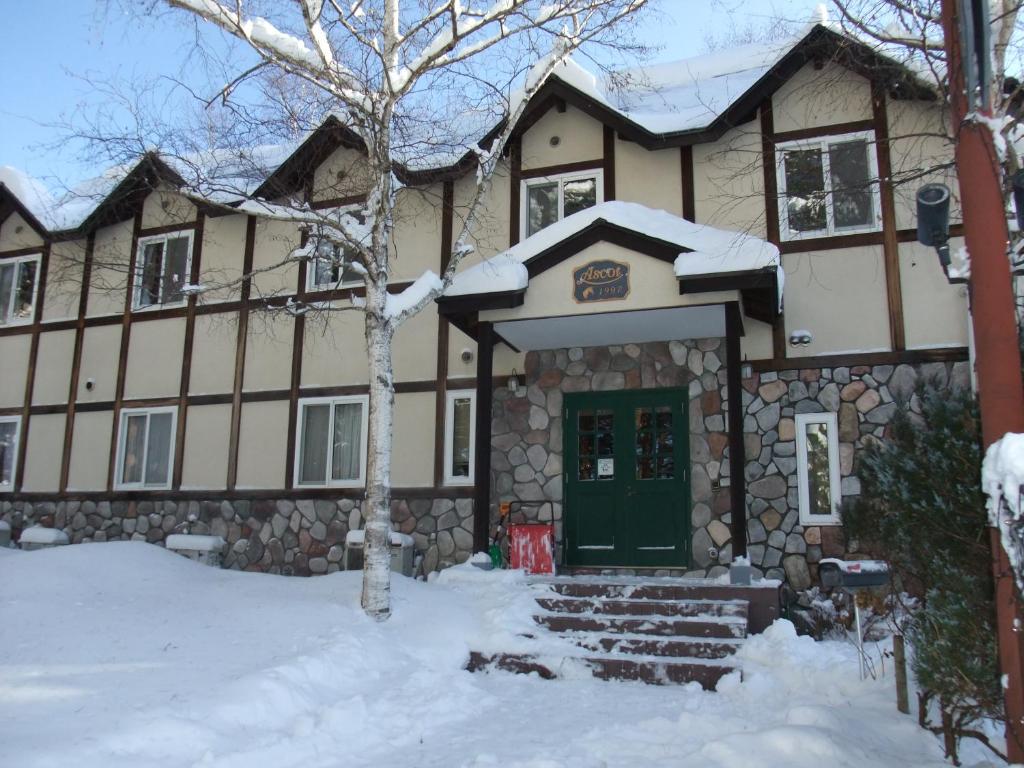 een huis met een groene deur in de sneeuw bij Gasthof Ascot in Hokuto