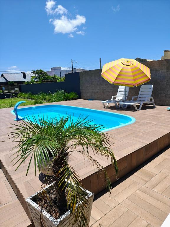 a swimming pool with a palm tree and an umbrella at Casa ,piscina há 100 metros do mar ,24 pessoas in Capão da Canoa