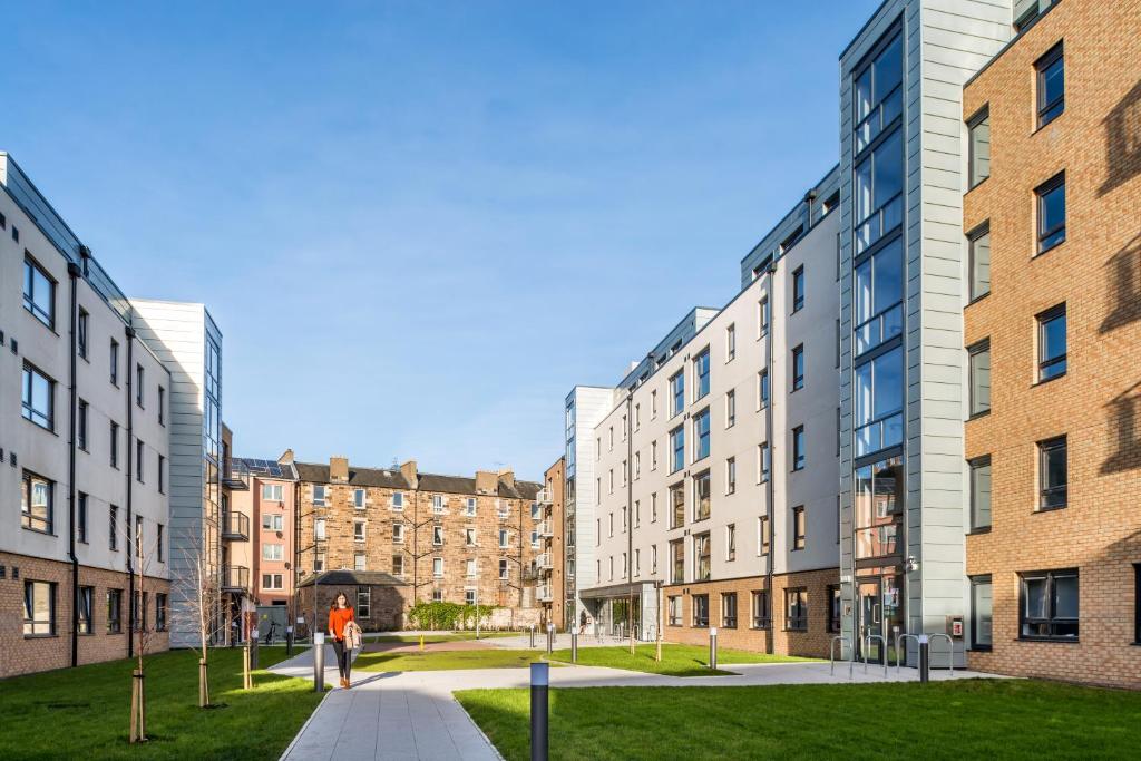 a person walking down a sidewalk in front of buildings at Destiny Student – Murano (Campus Accommodation) in Edinburgh