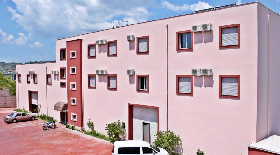 un edificio rosa con coches aparcados en un aparcamiento en Aurelis Hotel, en Bërxull