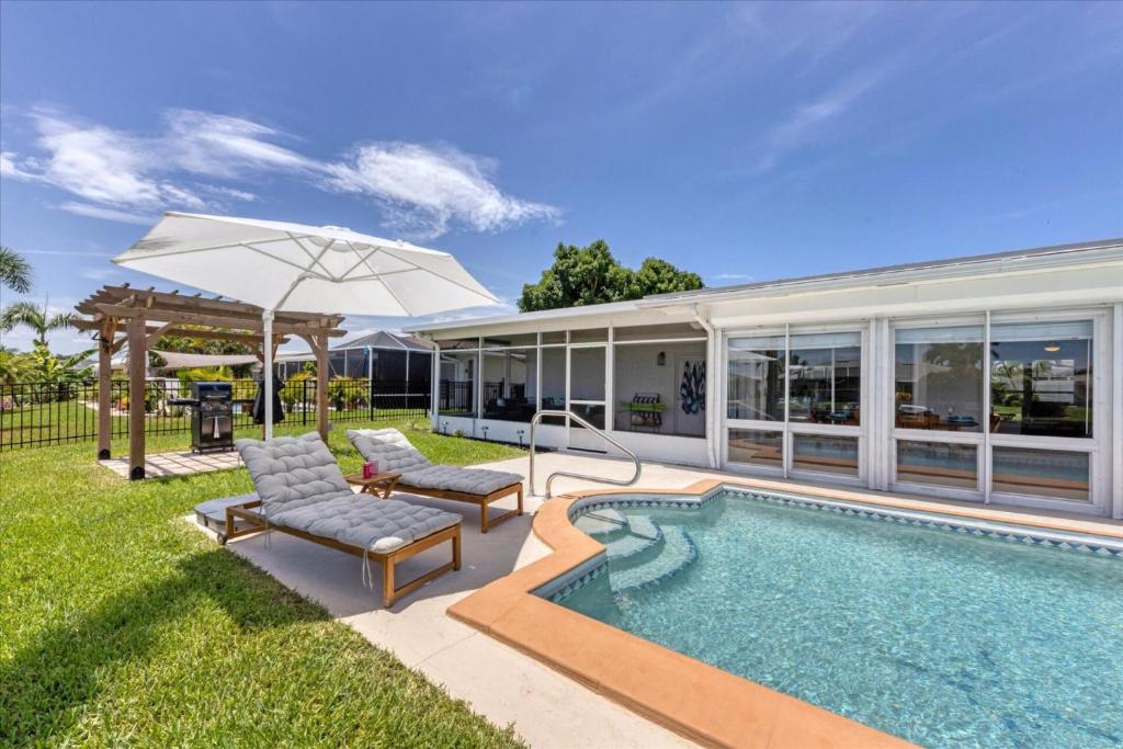a pool with two chairs and an umbrella next to a house at Relaxing Charlotte County Villa 5881 with Private Pool Access in Punta Gorda