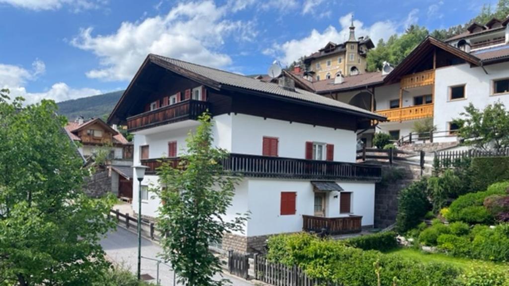 a white house with red windows on a hill at Apartments Goller in Ortisei