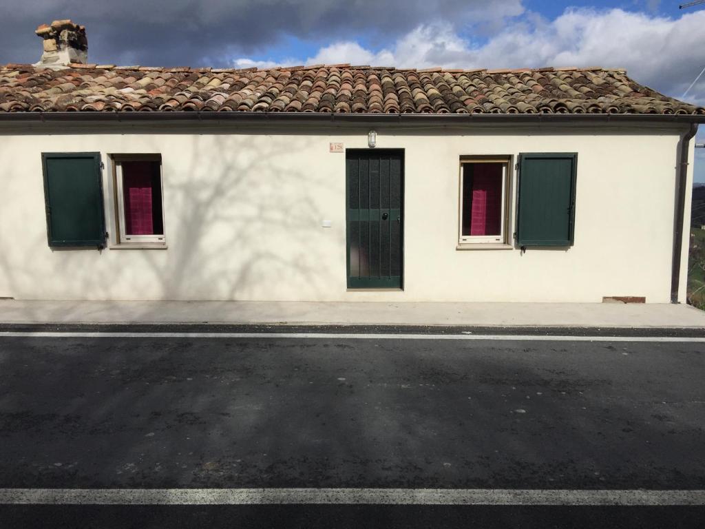 a white house with green windows and a street at Casa Matilde in Urbino