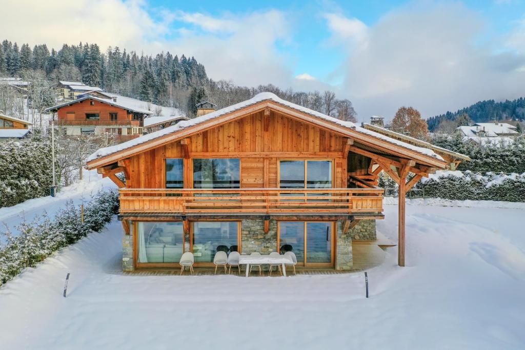 une maison en rondins avec trois personnes assises sur des chaises dans la neige dans l'établissement Chalet La Petite Forêt, à Megève