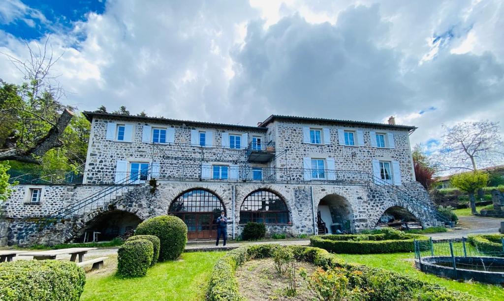 un grand bâtiment en pierre avec des fenêtres bleues et des buissons dans l'établissement Domaine de Souchiol, à Coubon