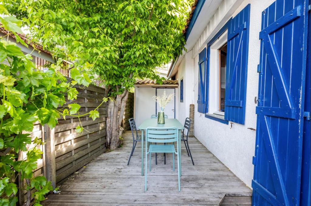 - une table et des chaises sur une terrasse couverte dotée de portes bleues dans l'établissement La Cabane 18 petit cocon de rêve, à Andernos-les-Bains