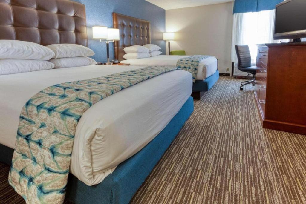 a hotel room with two beds and a television at Heritage Inn & Suites St Louis Fenton, Trademark by Wyndham in Fenton