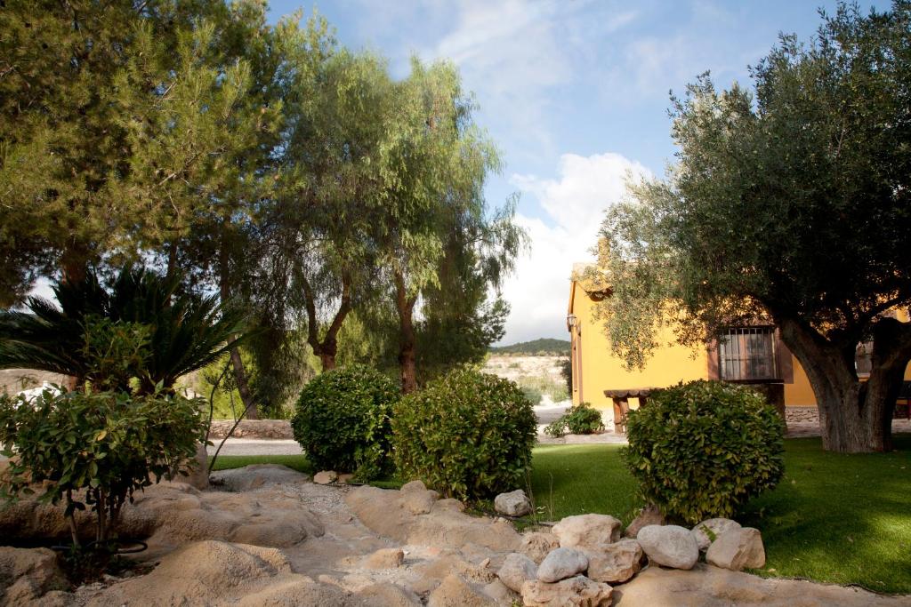 un jardín con rocas y árboles y una casa amarilla en El Mirador de Gebas, en Alhama de Murcia