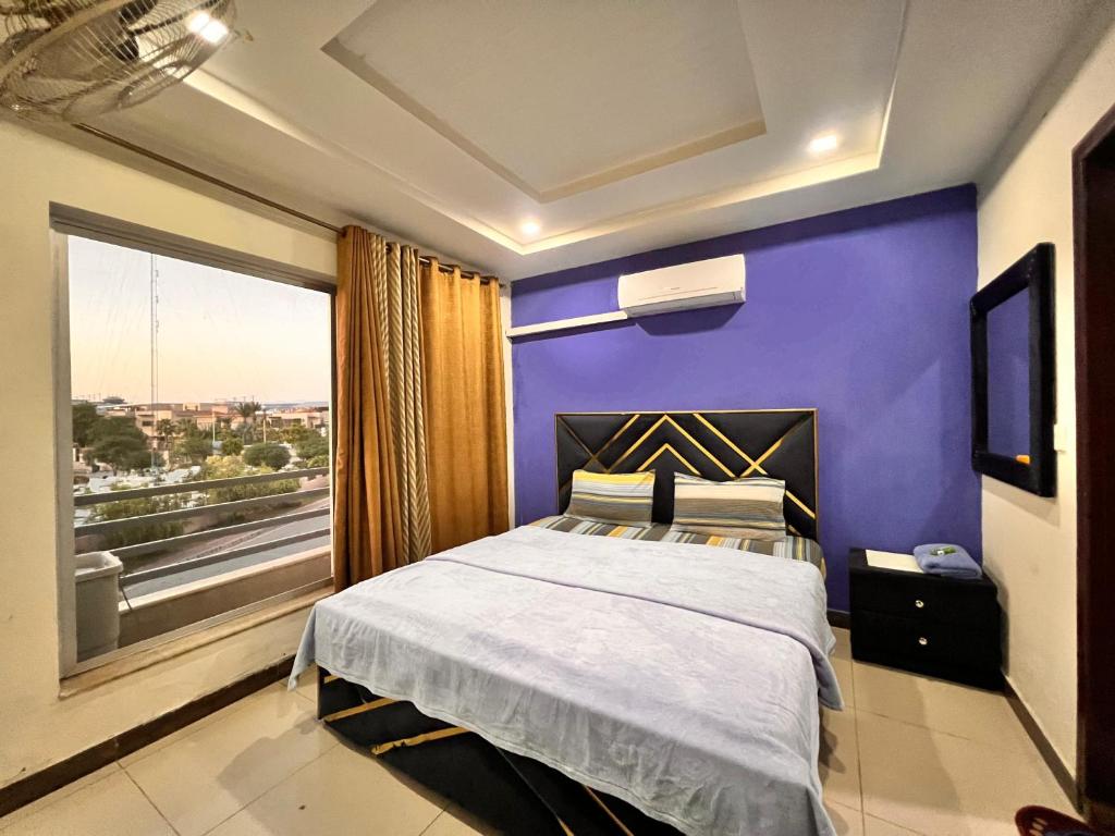 a bedroom with a purple wall and a bed with a window at Comfortable Apartment Bahria town Rawalpindi in Rawalpindi