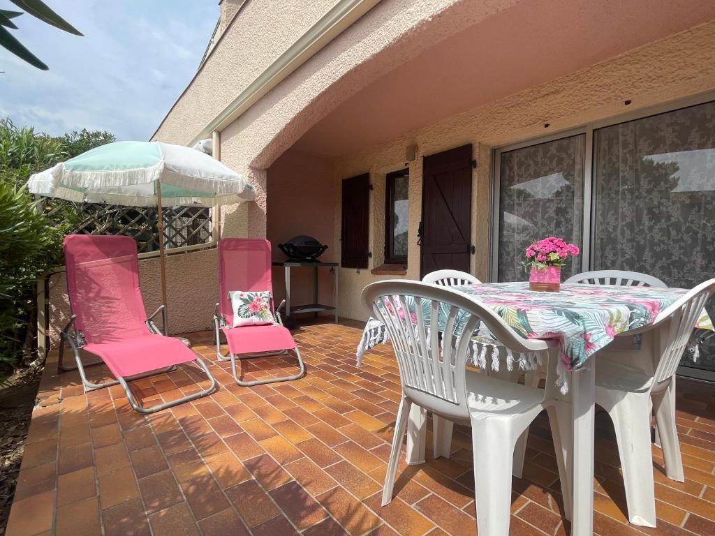 un patio avec une table, des chaises et un parasol dans l'établissement Rez-de-jardin Pinède Piscine Clim proche Plage Village naturiste, au Cap d'Agde