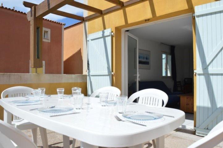 une table blanche avec des chaises blanches, des assiettes et des verres dans l'établissement NP230-040 Pavillon 3 pièces, Narbonne Plage, à Narbonne-Plage
