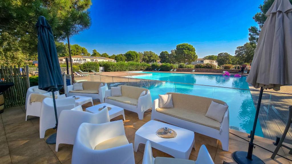 a swimming pool with white chairs and umbrellas next to a pool at Fiori Di Cala Rossa, Établissement CARDOGA Piscine, Mer & Montagne in Lecci
