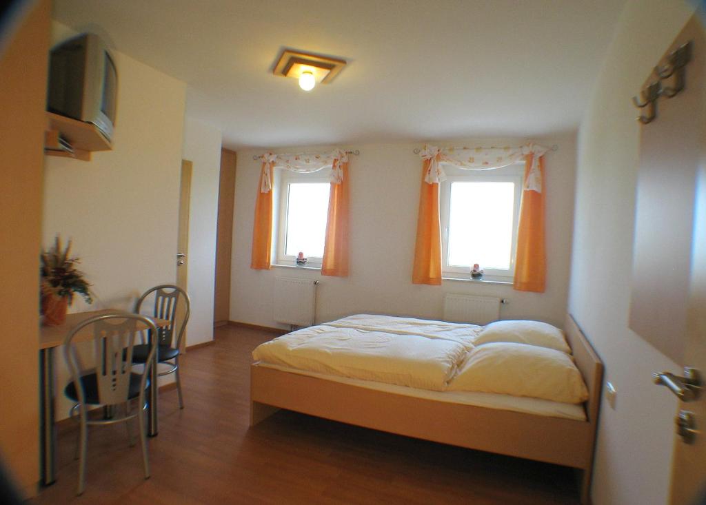 a bedroom with a bed and a table and two windows at Schirmer`s Hotelino in Röhrmoos