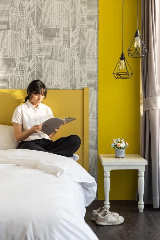 a woman sitting on a bed reading a book at 凝萃文旅 台中車站店 NCH-Business Hotel in Taichung
