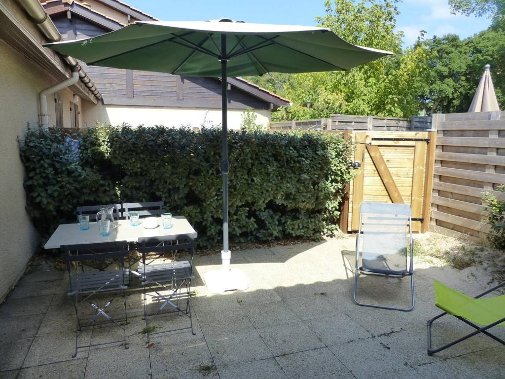 un patio avec une table et un parasol vert dans l'établissement Les Rives de Capbreton Villa patio Résidence pour 4 personnes, à Capbreton