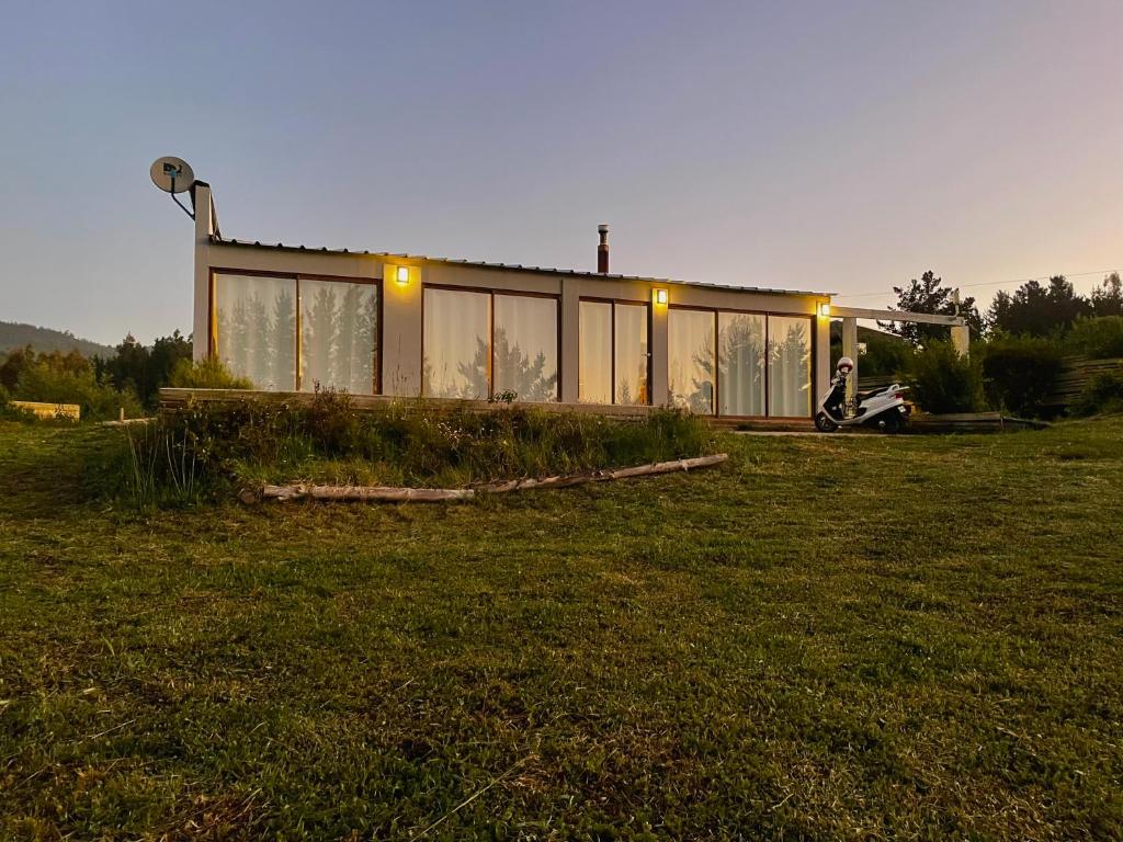 a house with glass windows on a field at Casa de campo in De Cauquenes