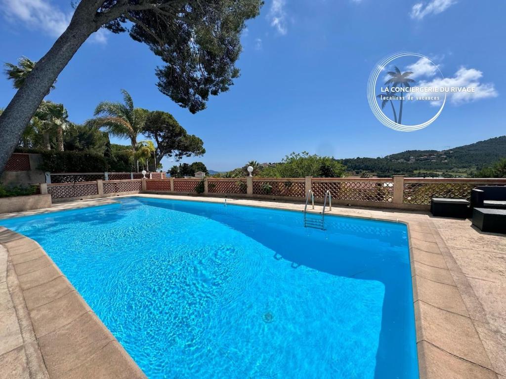 une piscine bleue avec un arbre en arrière-plan dans l'établissement Villa Le Sud - Piscine - Vue dégagée et aperçu mer, à Carqueiranne