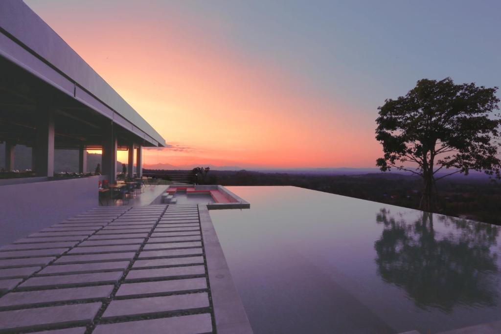 a sunset over a pool with a tree on a building at The Paz Khao Yai in Nong Sarai