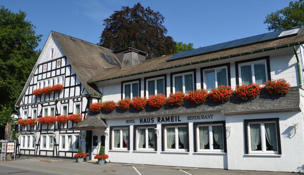 Un bâtiment blanc et noir avec des fleurs rouges sur lui dans l'établissement Hotel Haus Rameil, à Lennestadt