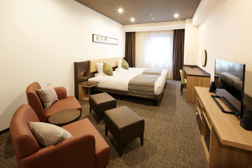 a hotel room with a bed and chairs and a television at HOTEL MYSTAYS PREMIER Kanazawa in Kanazawa