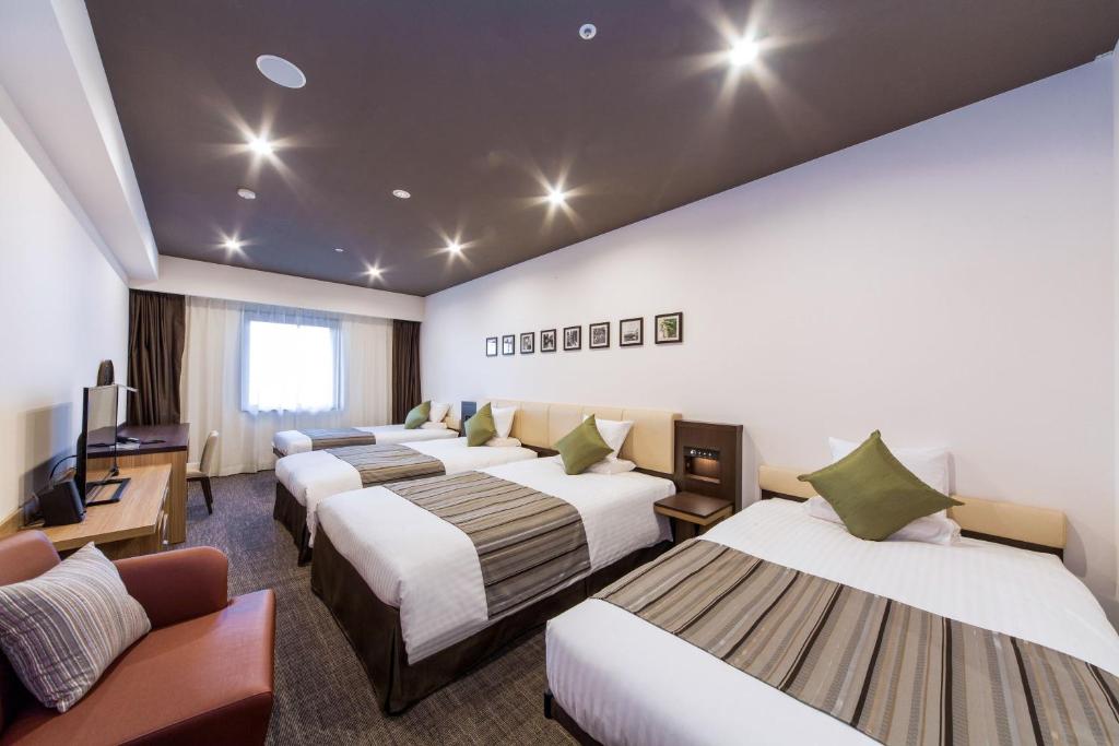 a hotel room with four beds and a flat screen tv at HOTEL MYSTAYS PREMIER Kanazawa in Kanazawa