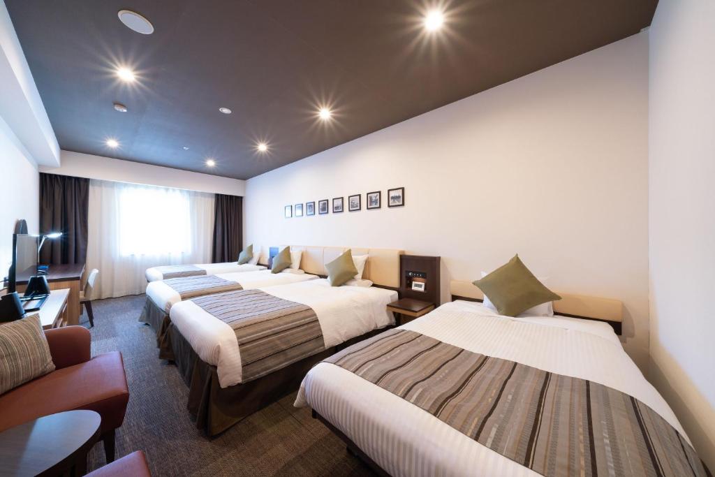 a hotel room with four beds and a desk at HOTEL MYSTAYS PREMIER Kanazawa in Kanazawa